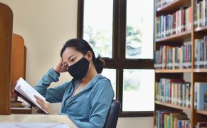 Woman with protective mask studying in library